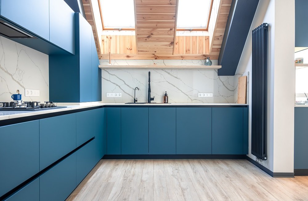 Corner attic kitchen with matte blue cabinets, light wood accents, and Scandinavian aesthetic. Bright, ergonomic and stylish cooking area with natural light.